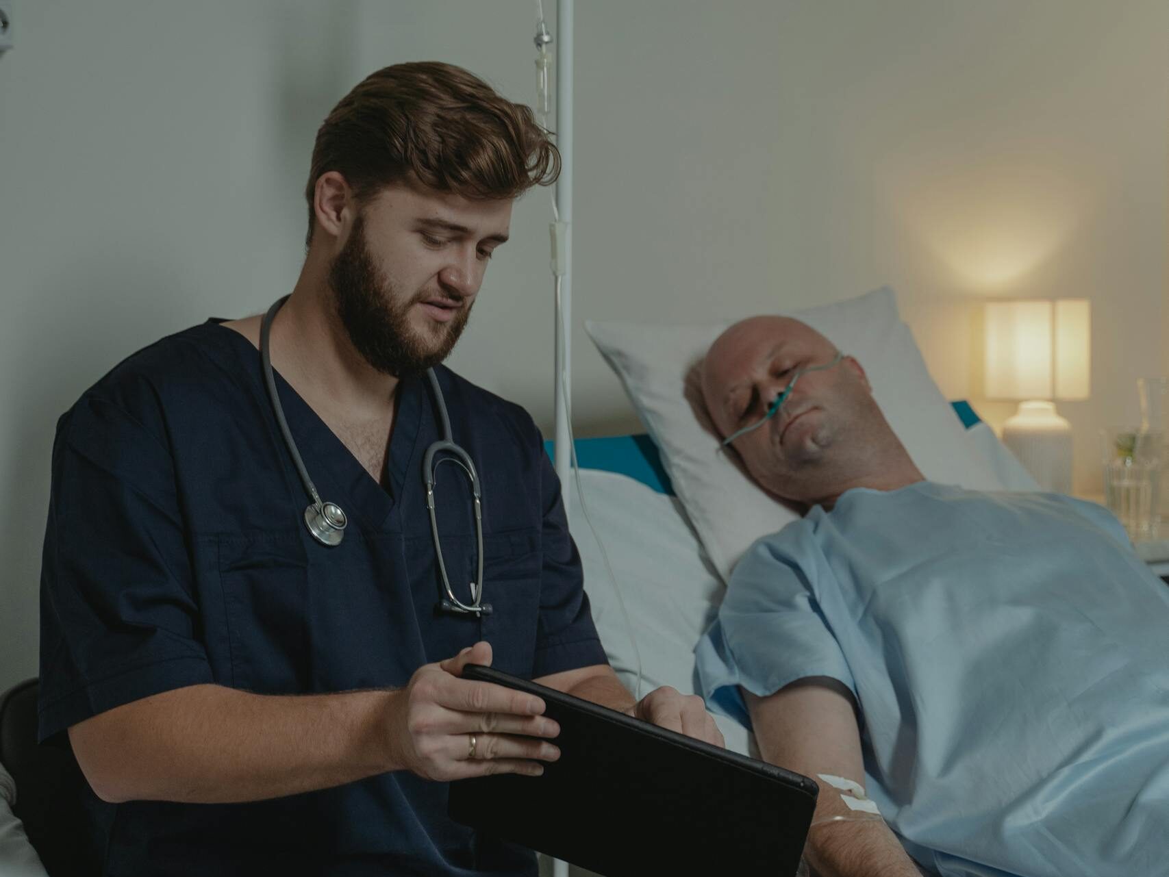 A doctor in a scrub suit caring for a patient in a hospital bed.