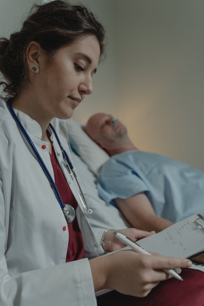 A female doctor takes notes beside a patient in a hospital room, showcasing medical care.