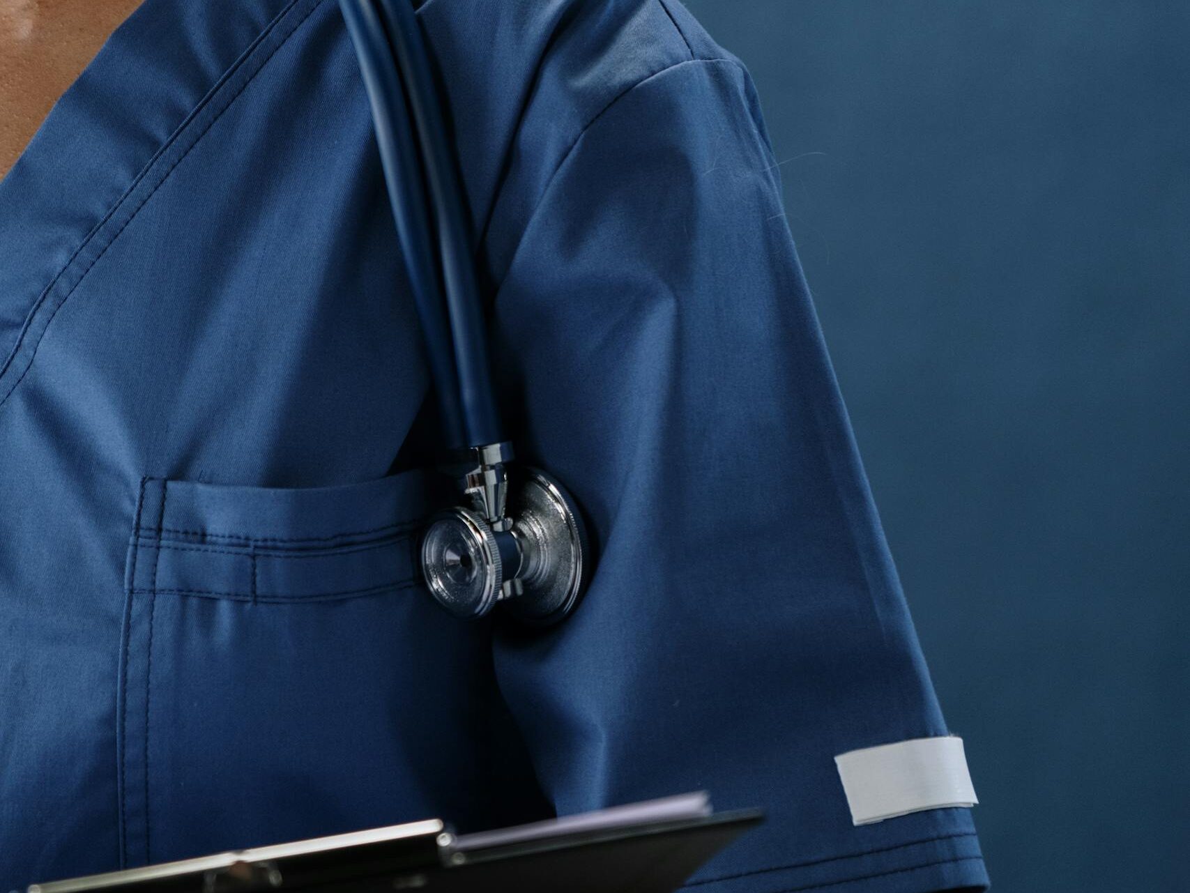 Close-up of a healthcare professional in blue scrubs with a stethoscope and clipboard.
